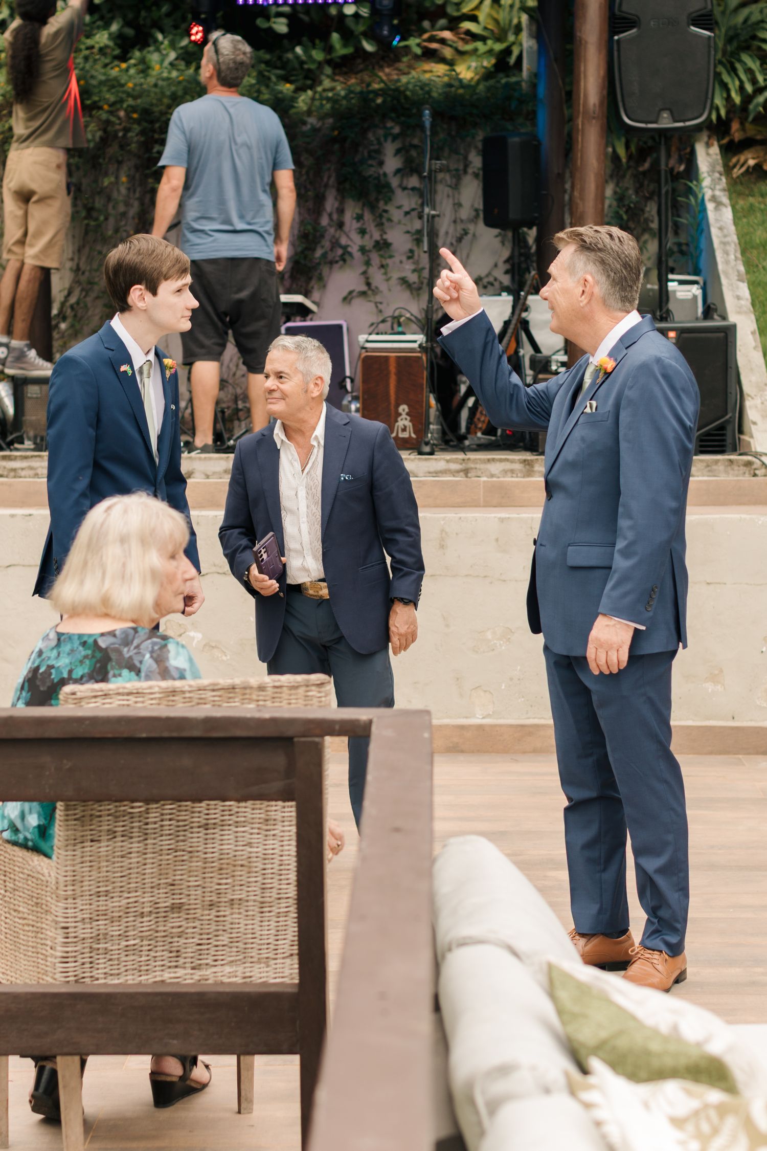 Wedding party mingles on an outdoor patio with wicker furniture and tropical landscaping.