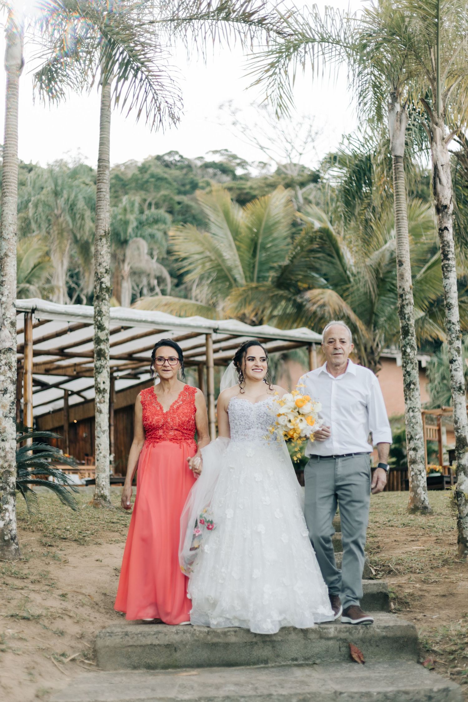 A wedding party poses under palm trees at a tropical outdoor venue.