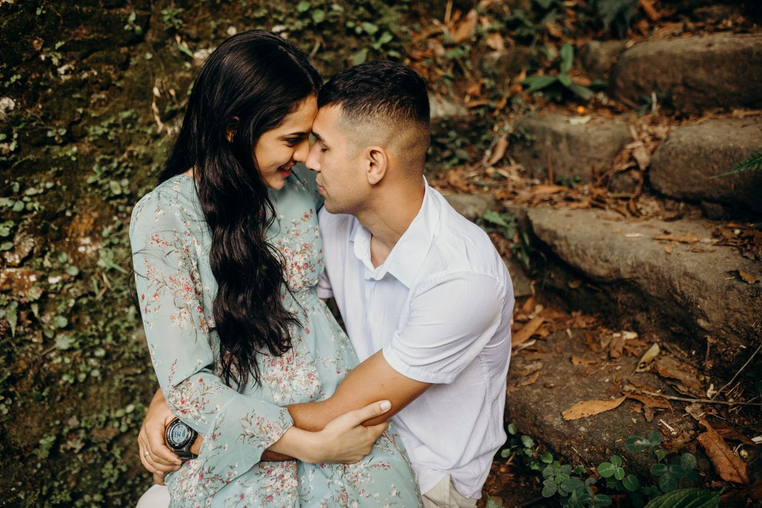 Romantic couple in casual attire share an intimate moment on stone steps surrounded by autumn foliage.