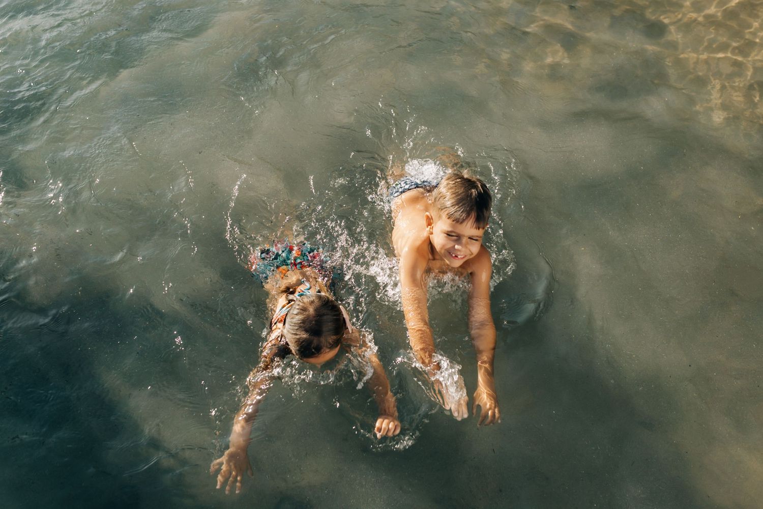 Two swimmers creating splashes while playing in turquoise ocean water.