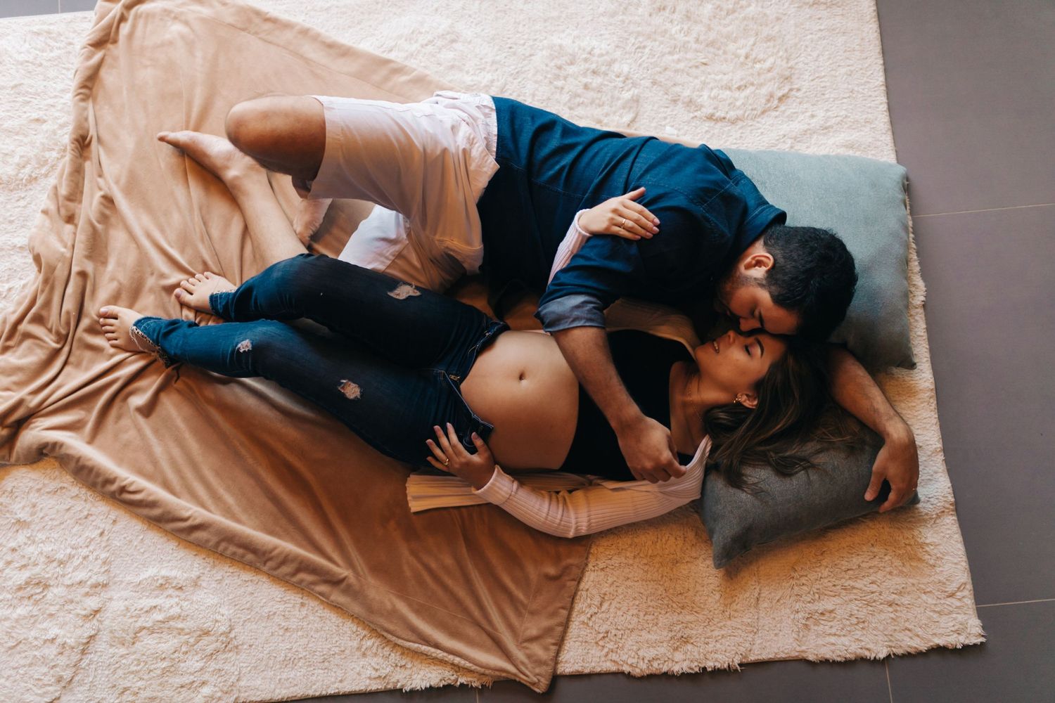 A couple cuddles together on a cozy beige blanket with their grey cat.