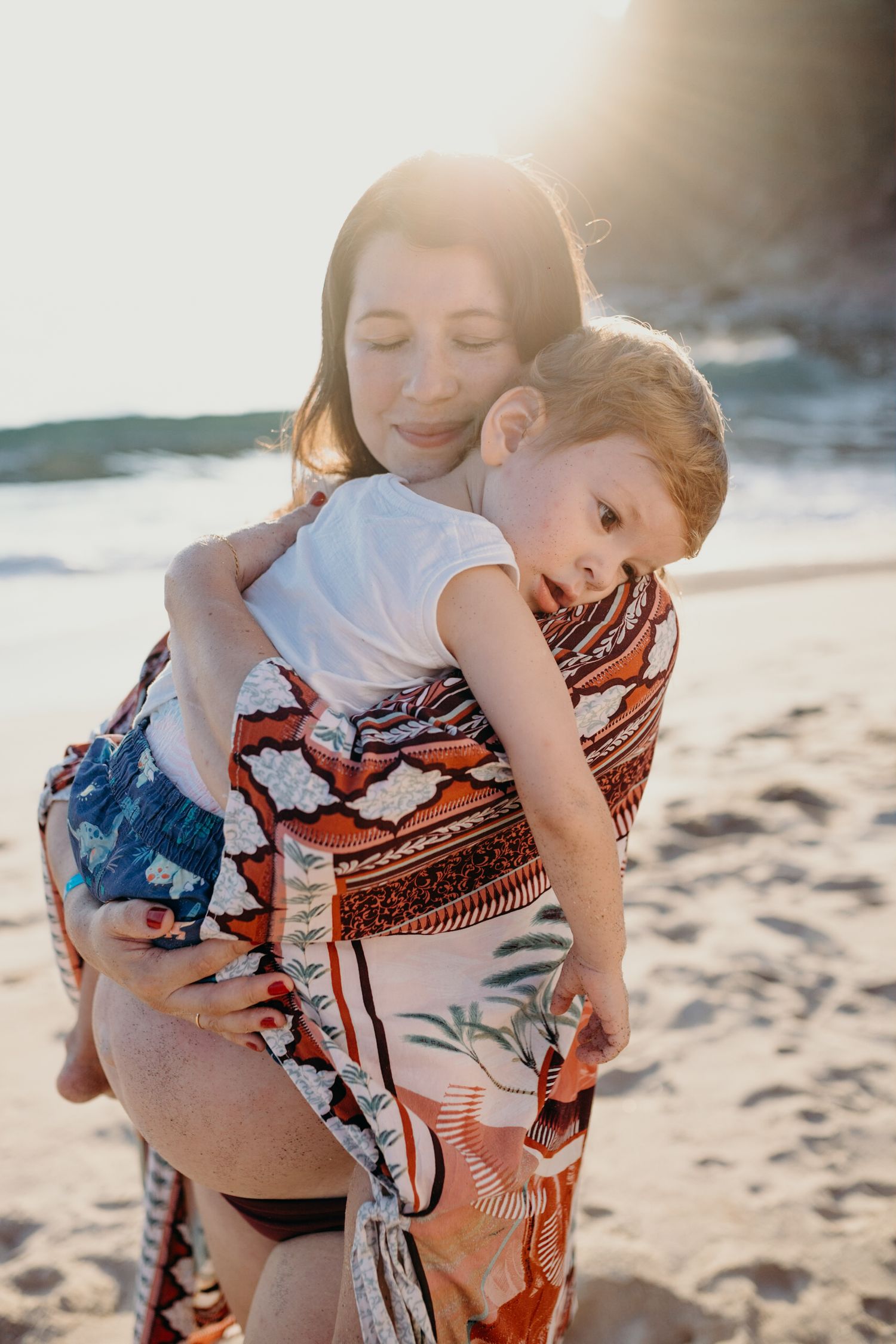 Family enjoying a tender moment together on a sunny beach with colorful printed fabric wrap.