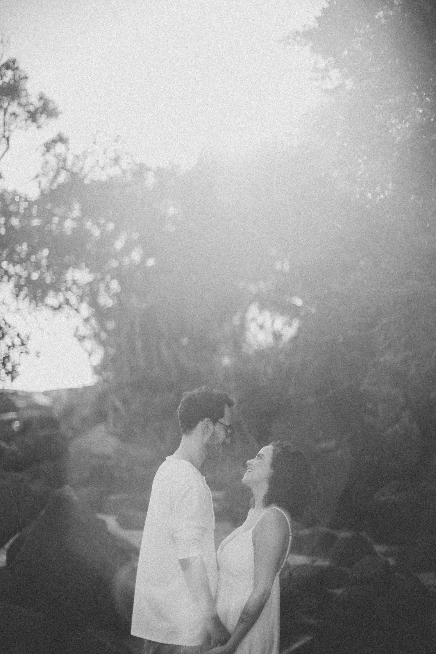 Black and white portrait of couple gazing at each other against natural backdrop.