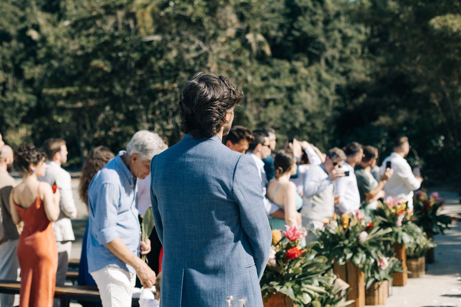 Wedding guests gather outdoors beneath string lights at a rustic venue.
