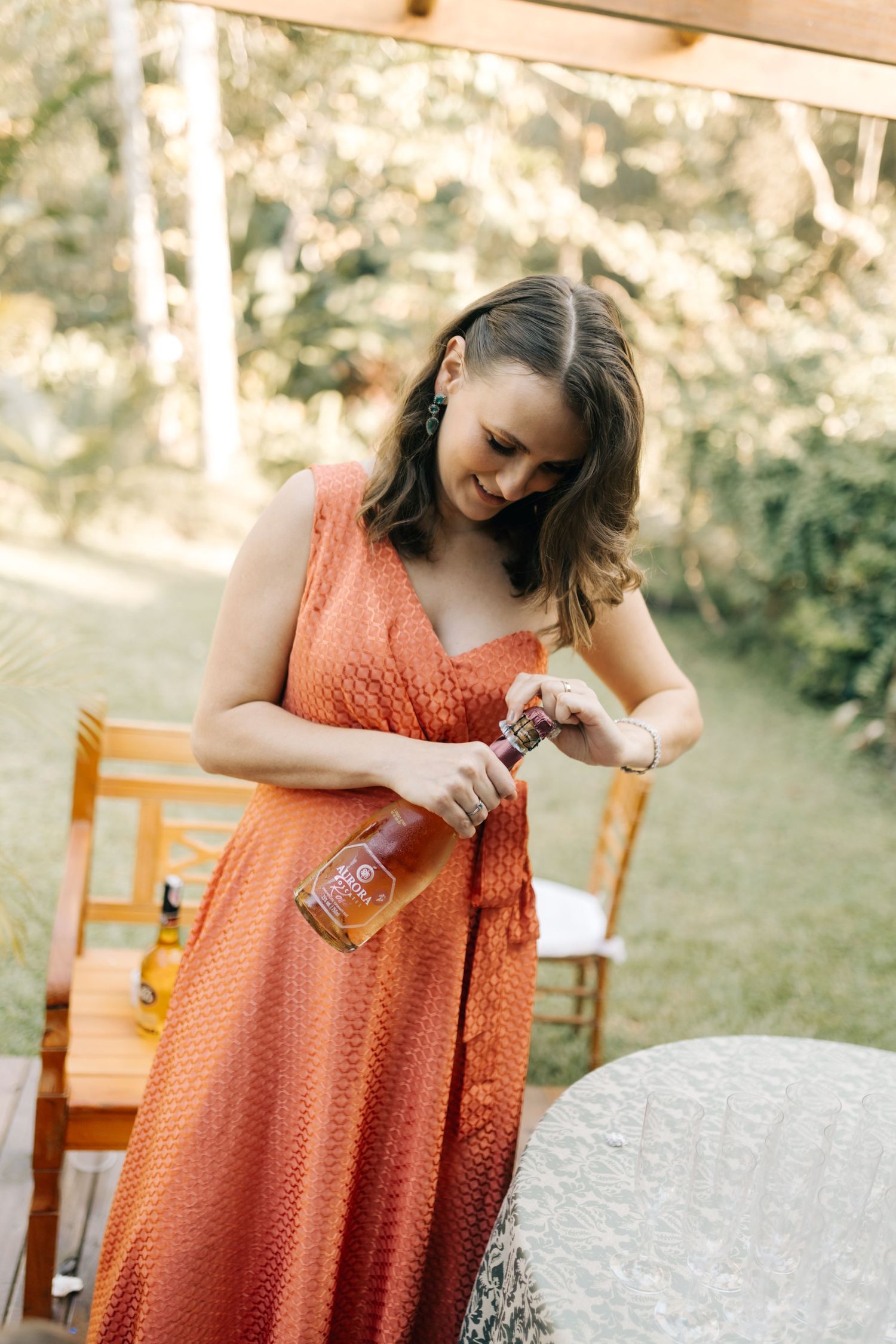 Three people in coral-colored dresses laugh together outdoors on a sunny day.