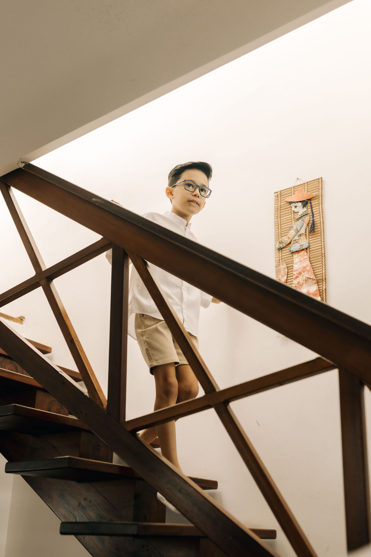Person in casual wear standing on wooden stairs looking down through railing.