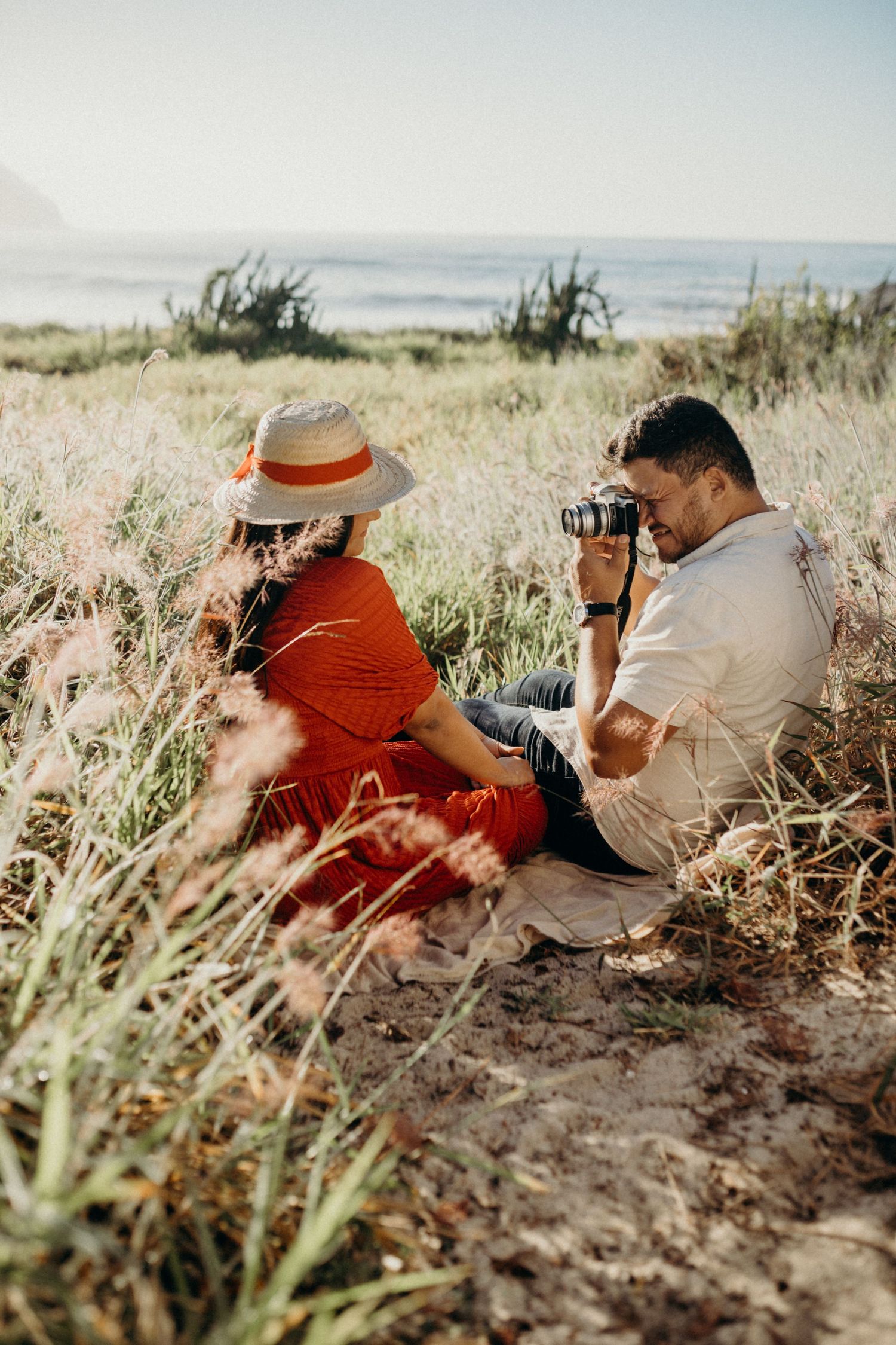 Photographer taking pictures of subject in red dress near coastal landscape.