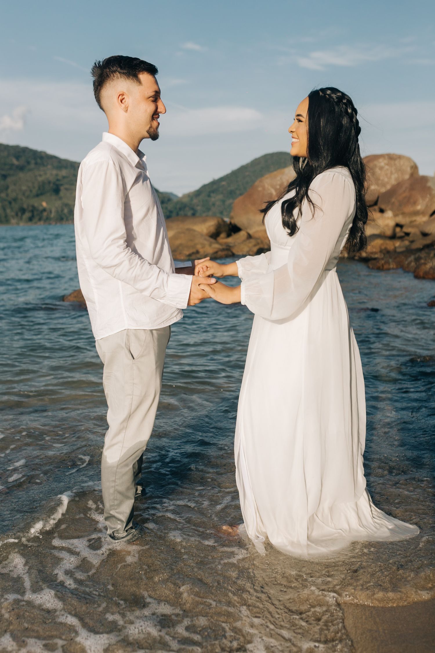 A couple shares an intimate moment while standing in shallow water with mountains in the background.