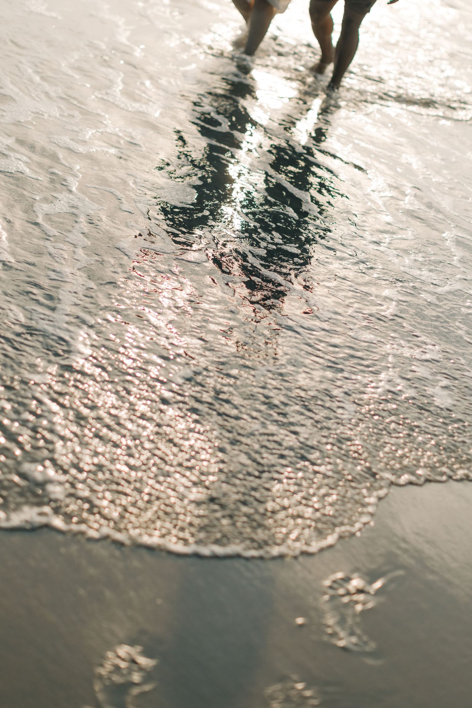Reflections of legs in shallow water on a sunlit beach.
