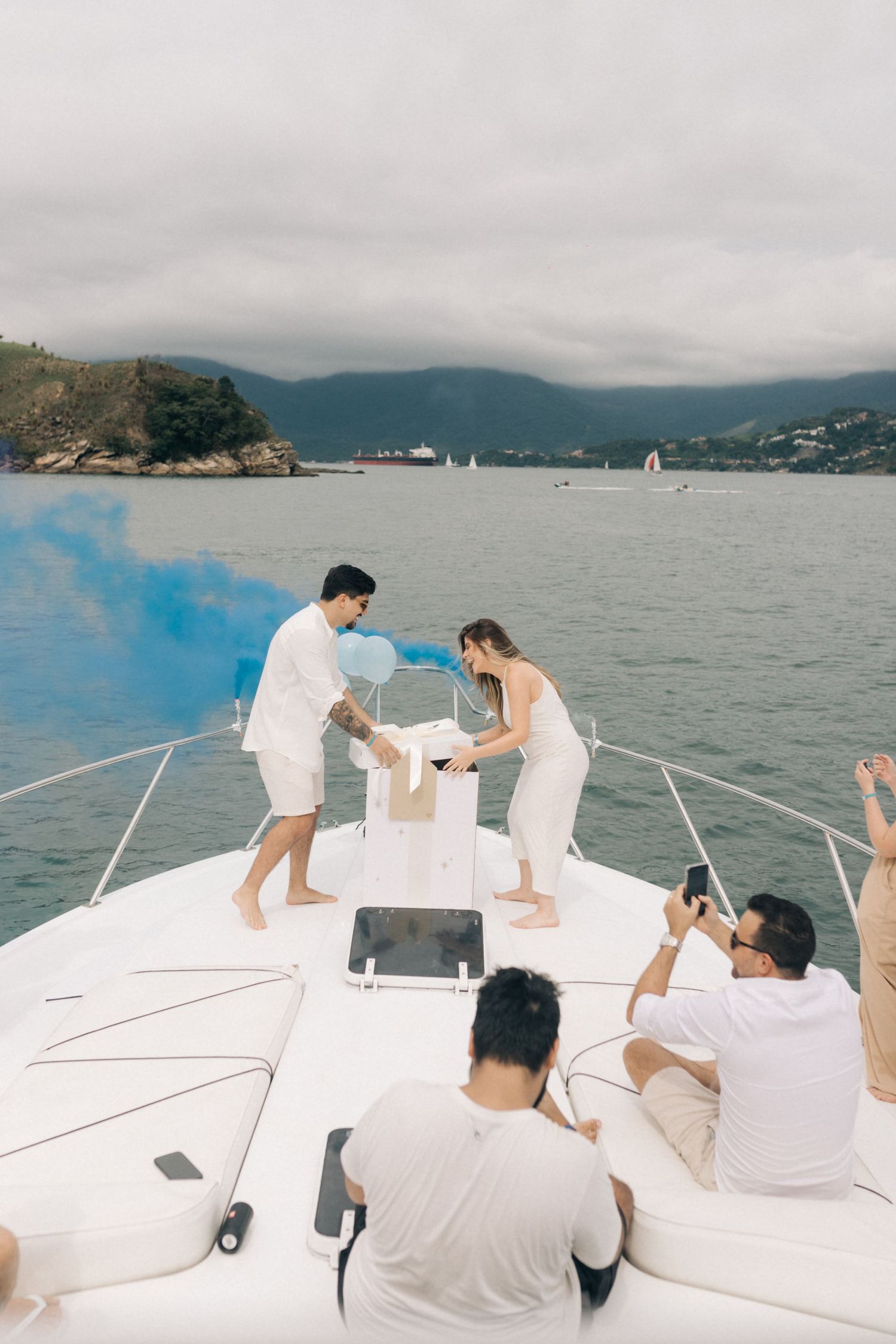 Intimate celebration on a boat's bow with mountains and cloudy skies in the background.