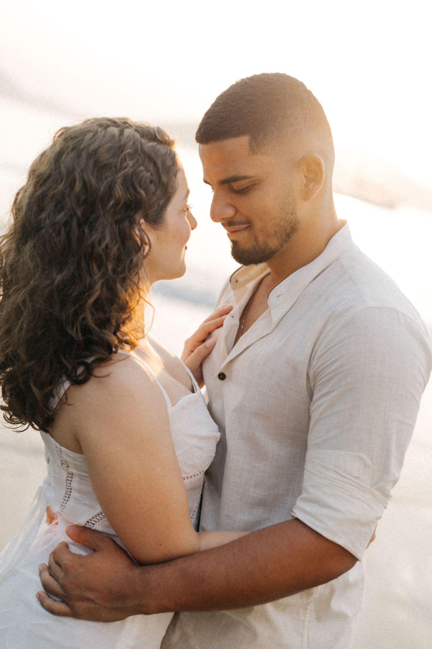 A romantic couple shares an intimate moment in white clothing during sunset.