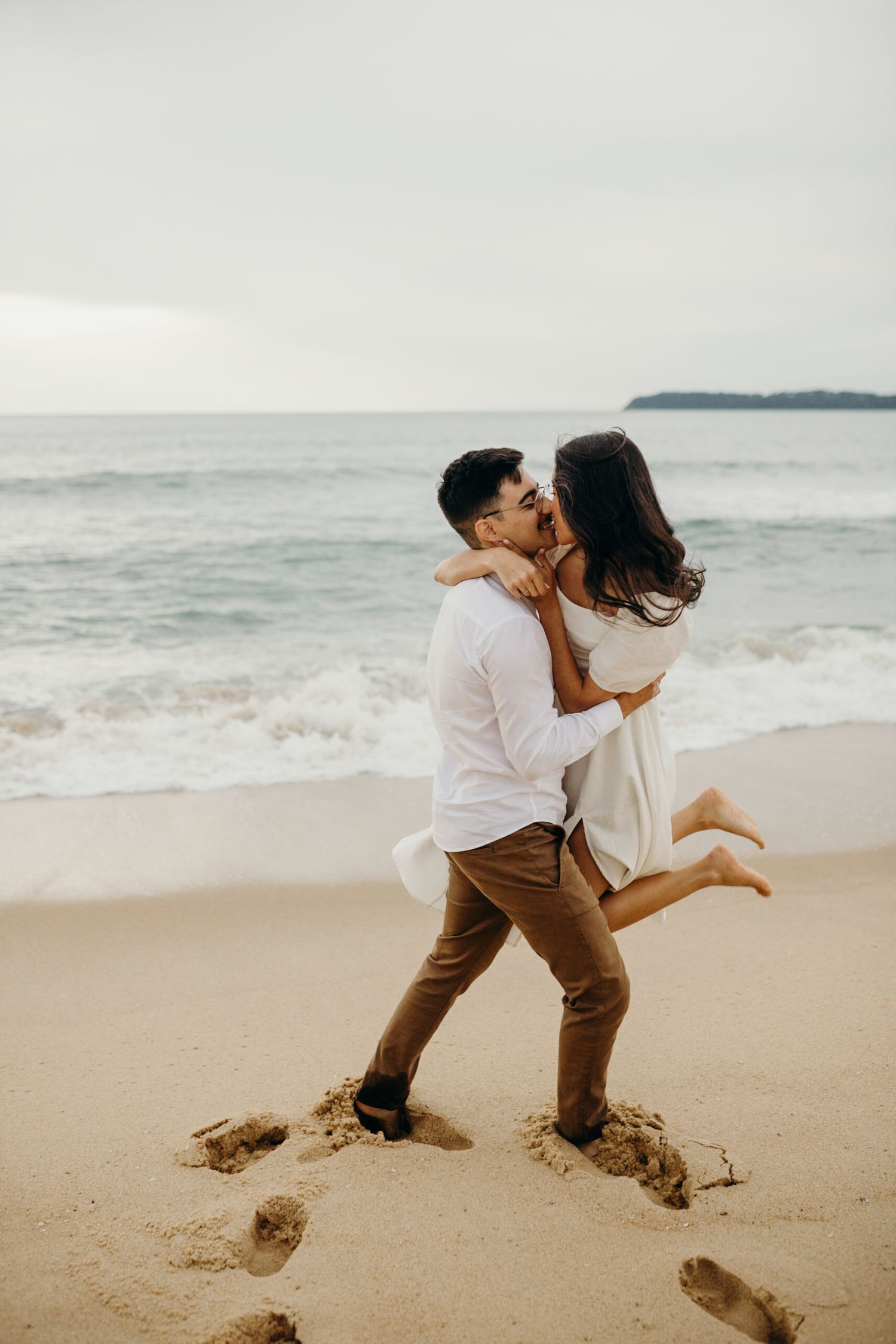 A playful beach photo with one person lifting the other against an ocean backdrop.