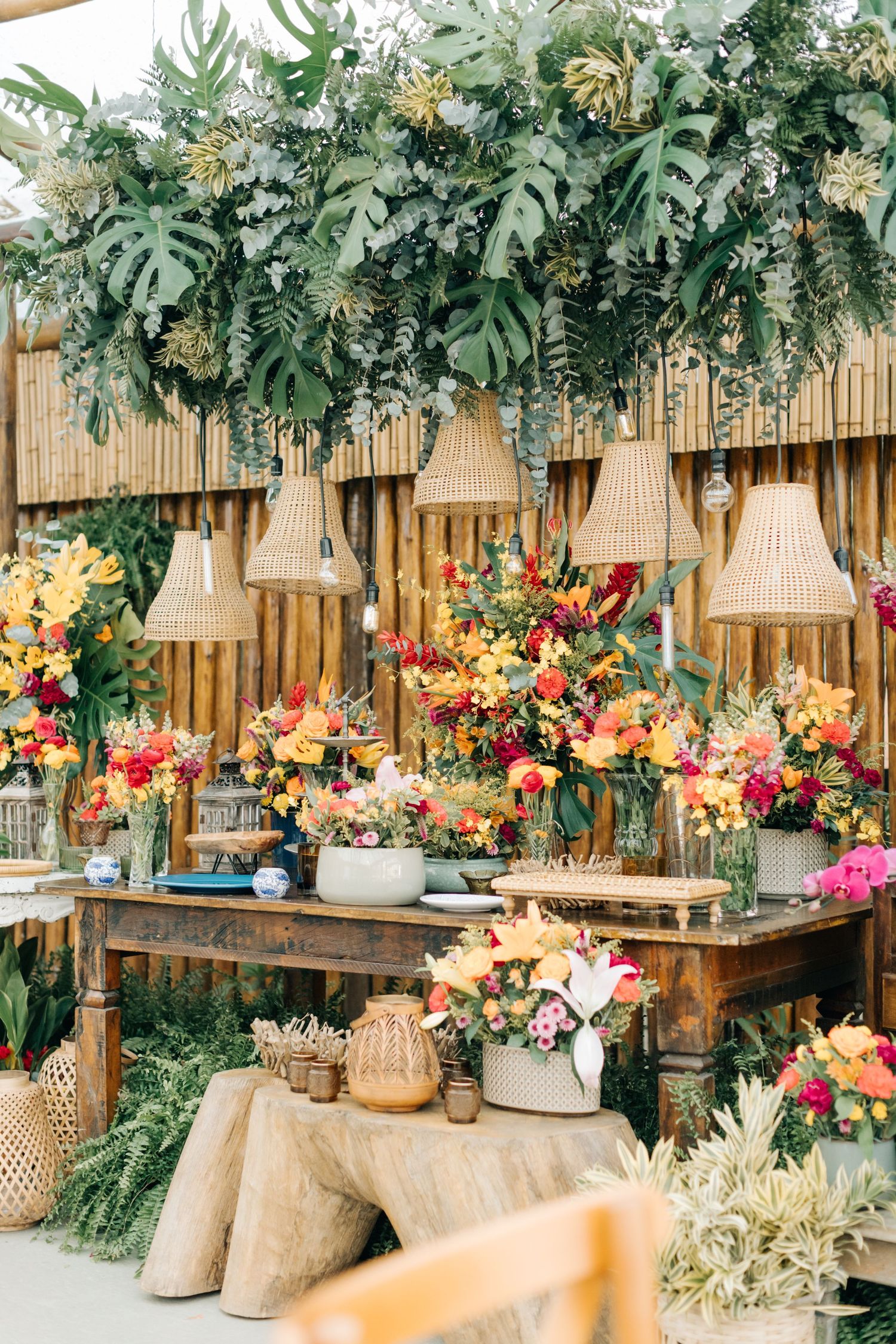 Tropical wedding decor featuring monstera leaves and bright colorful flowers on wooden tables.