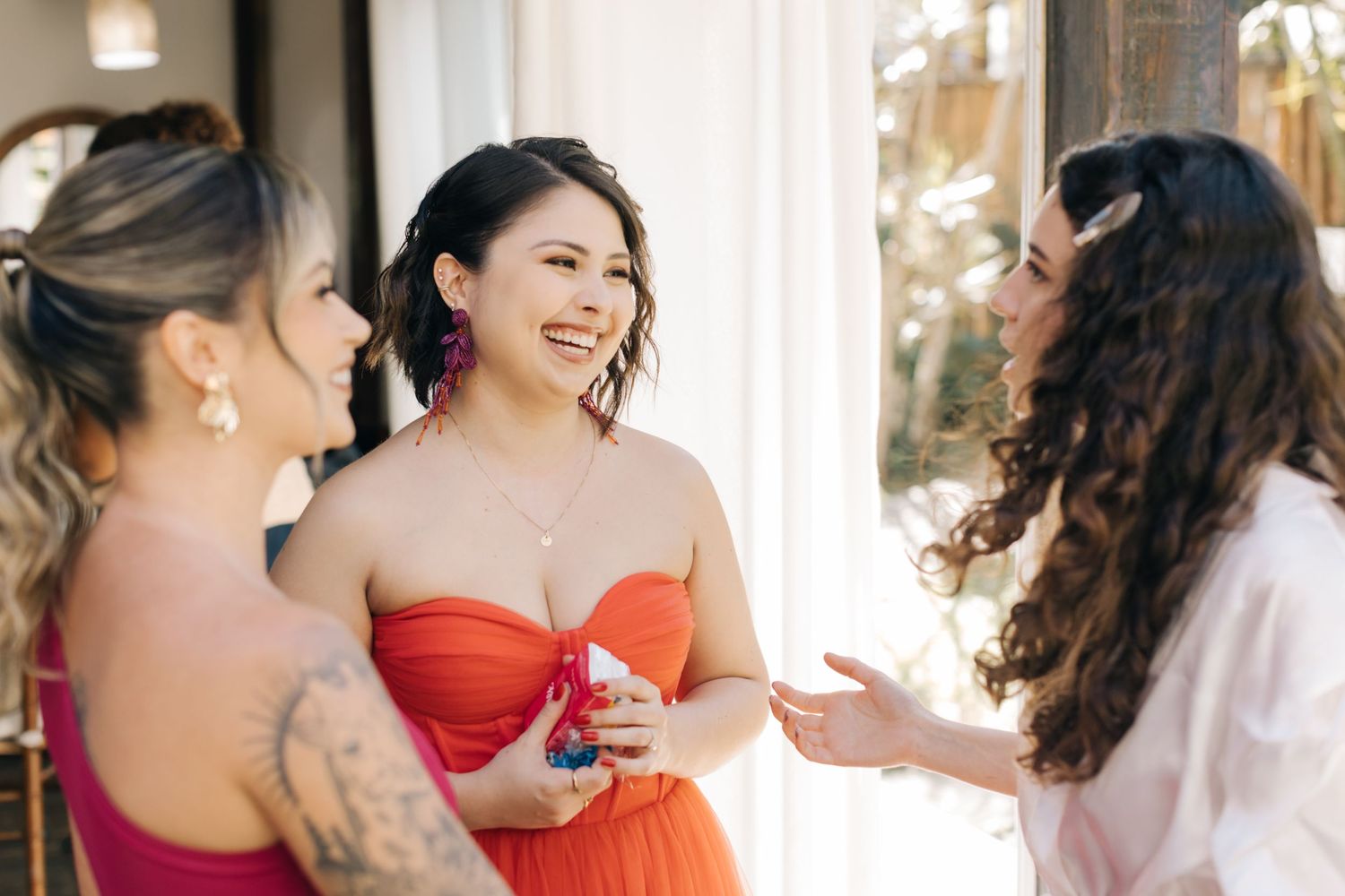 Wedding preparation scene with people in formal red dresses sharing a laugh.