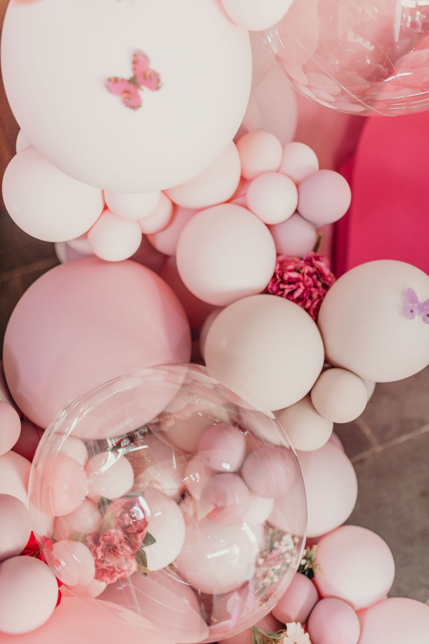 Pink and white balloon arrangement with butterfly decorations and clear bubble balloons.