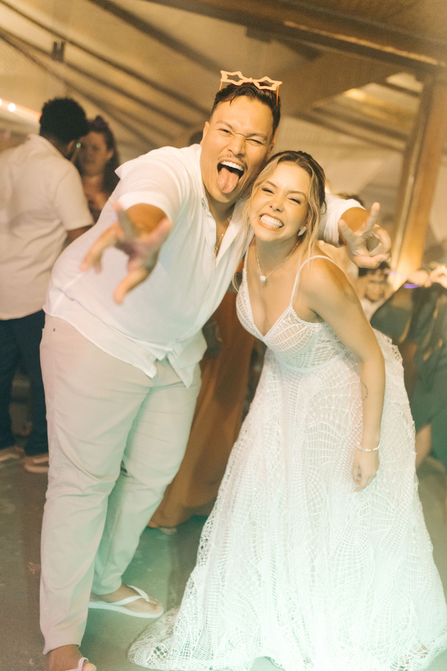 Wedding reception celebration with couple dancing and laughing in matching white outfits.