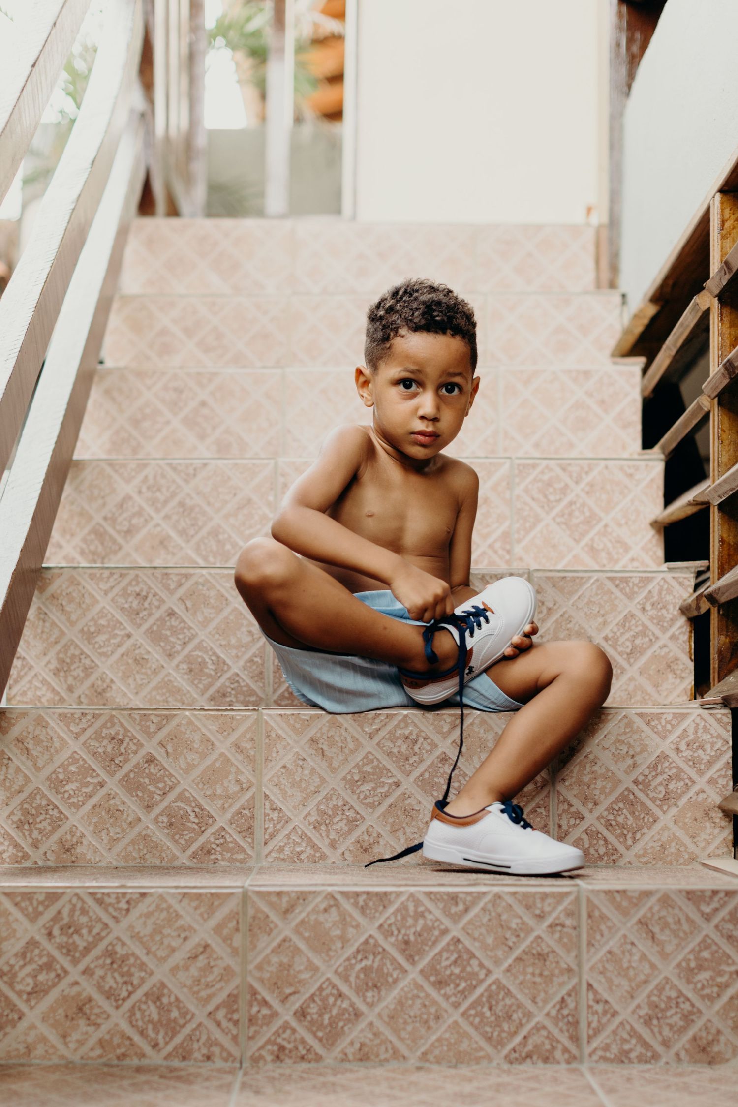 Small child sitting on tiled steps learning to put on shoes independently.