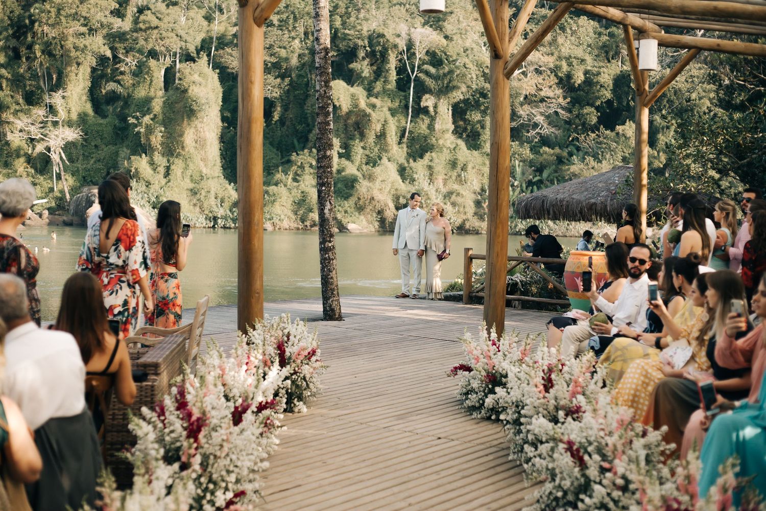 Wedding ceremony setup with wooden pergola and floral aisle decorations overlooking a serene lake.