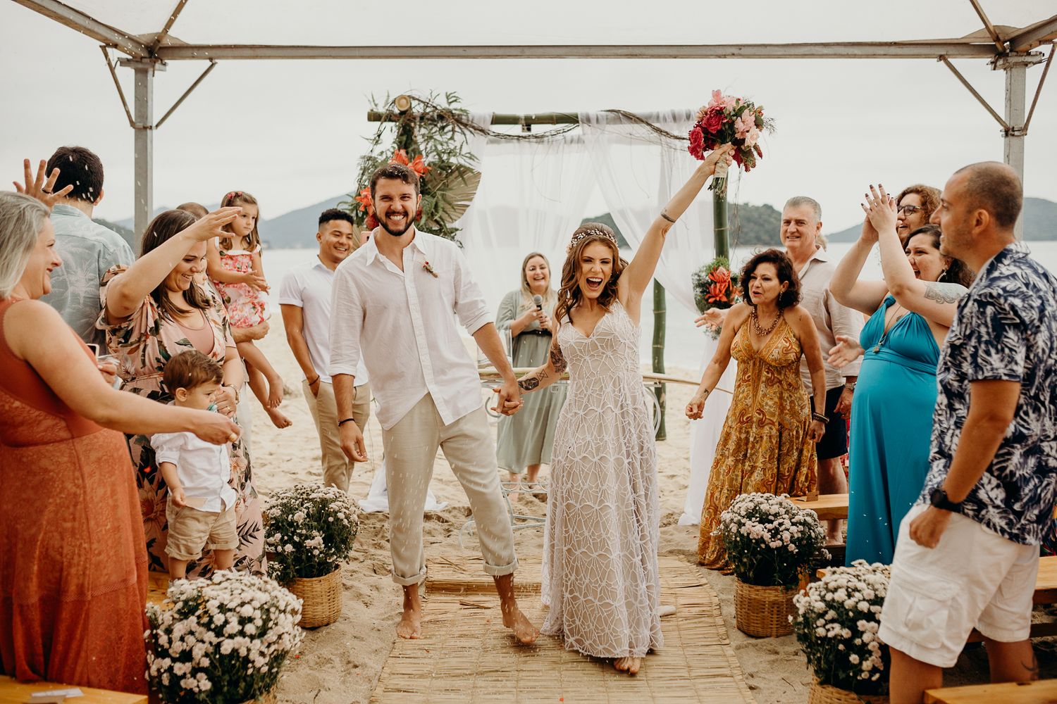 A victorious celebration moment during a beach wedding with guests cheering.