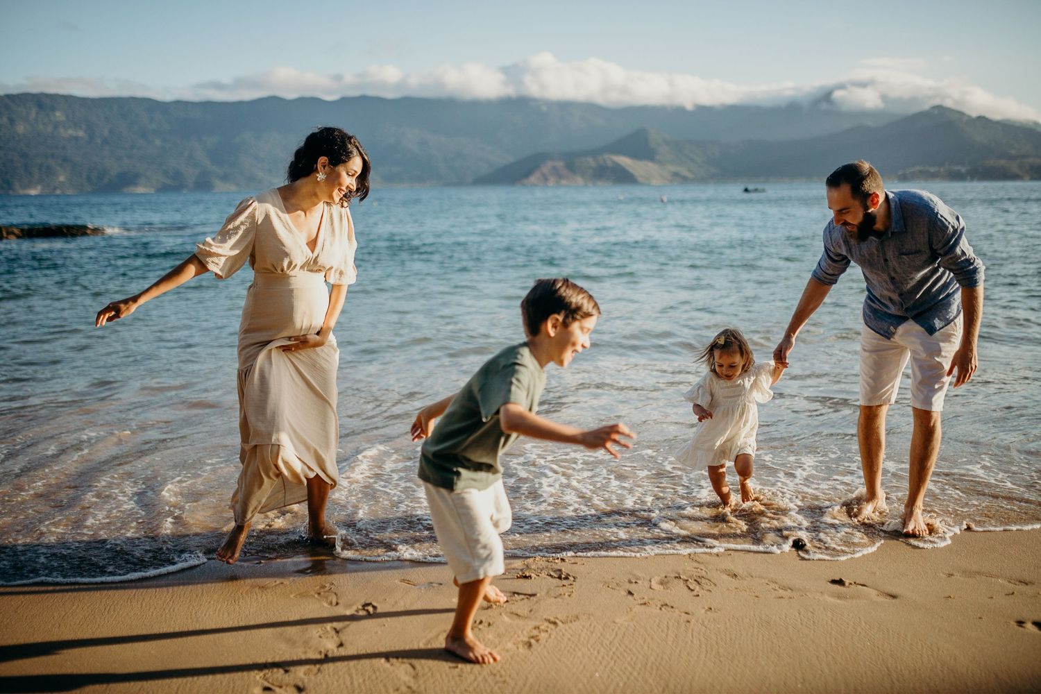 Family playing together in the surf with mountain backdrop at golden hour.