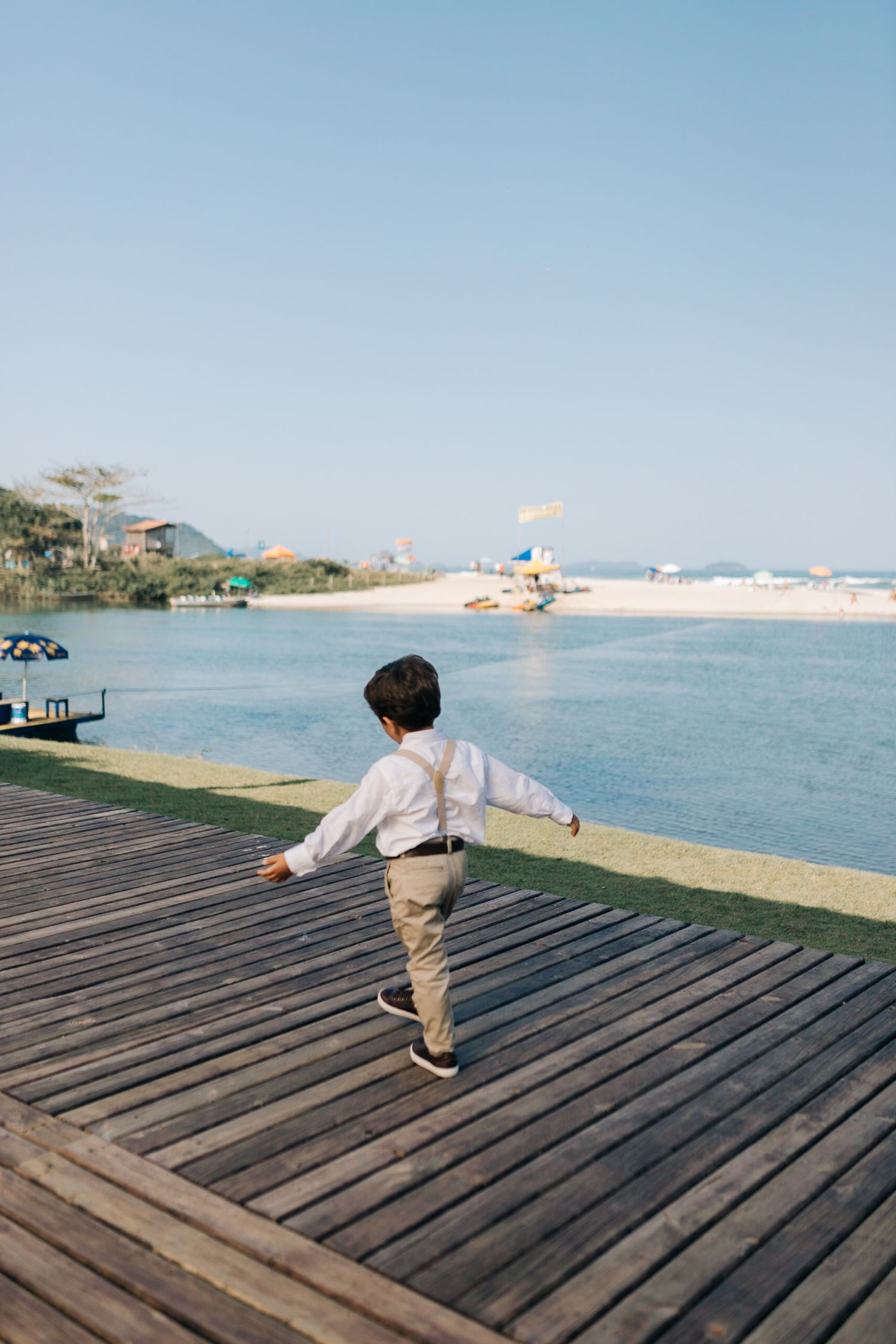 Young child running on wooden boardwalk by waterfront on sunny day.