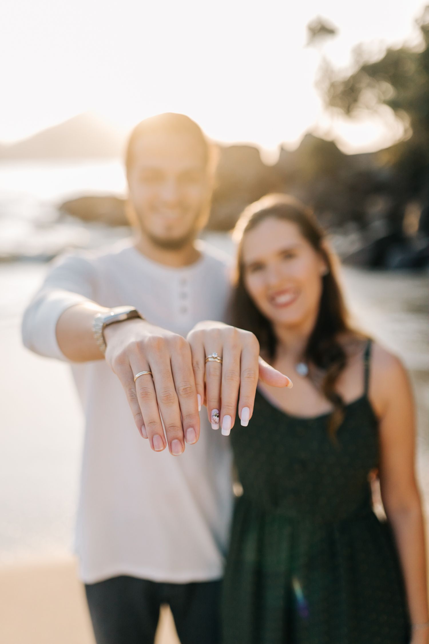 Newly engaged couple showing off engagement ring during sunset photoshoot at the beach.