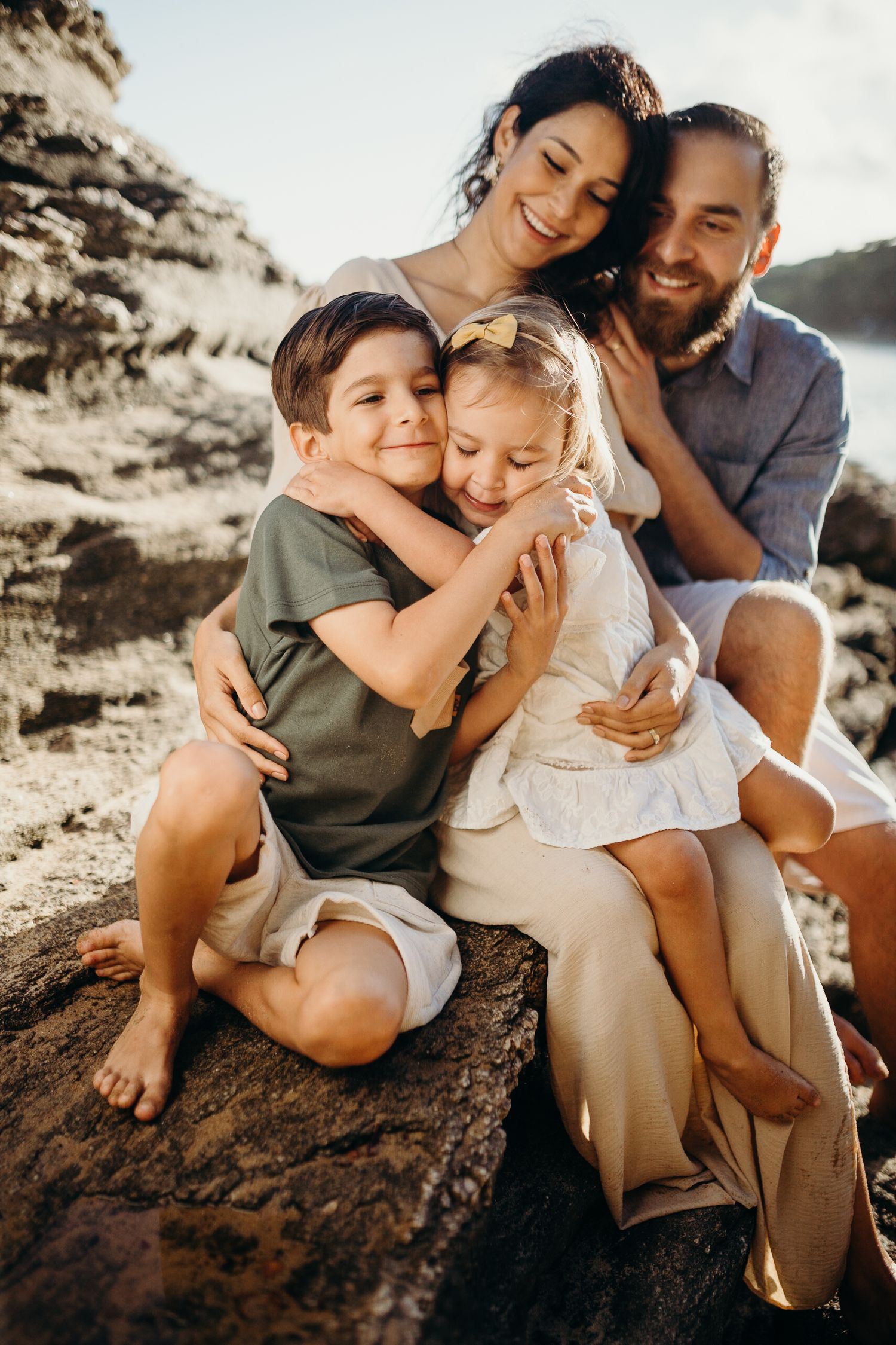 A family shares tender moments together on a rocky beach during a warm sunset photoshoot.