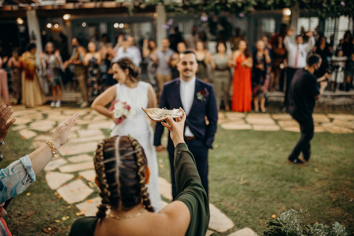 Outdoor wedding ceremony with guests standing on grass and stone pathways.