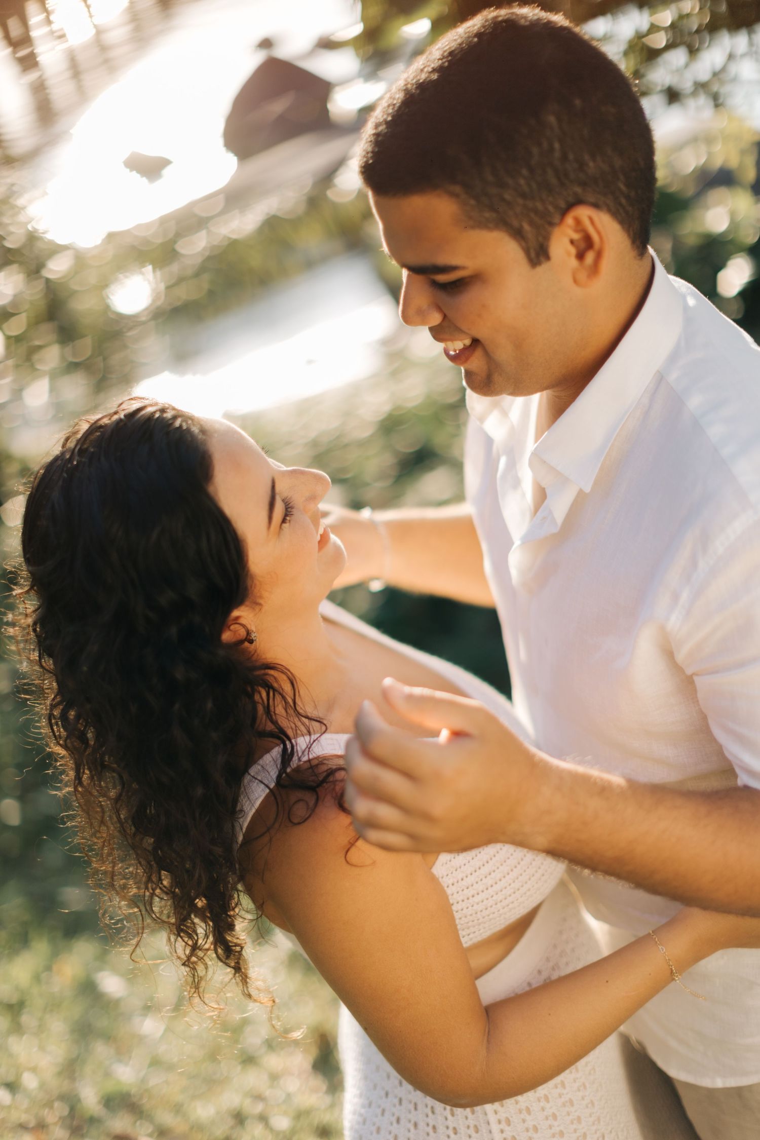 Couple in white clothing shares intimate embrace during golden hour photoshoot.