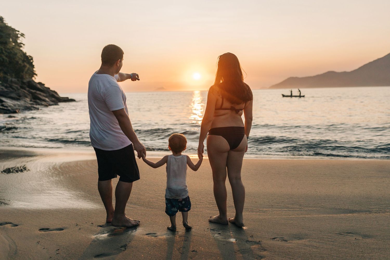 Family holding hands while walking along beach shore at sunset.