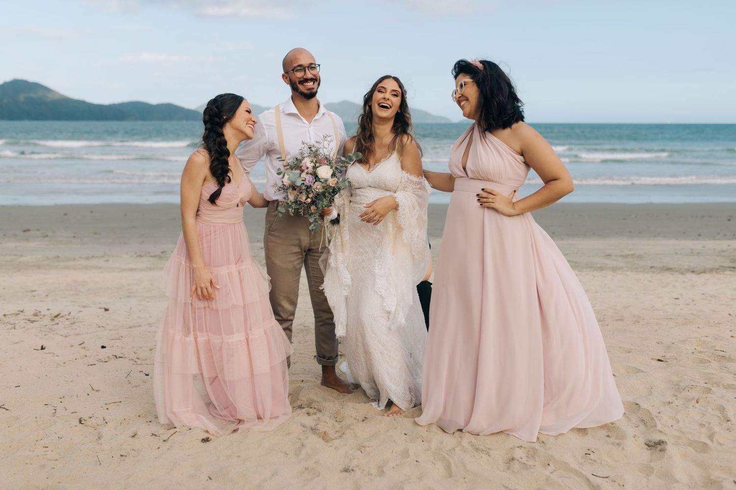 Bridal party laughing and posing candidly on sandy beach during sunset photo session.