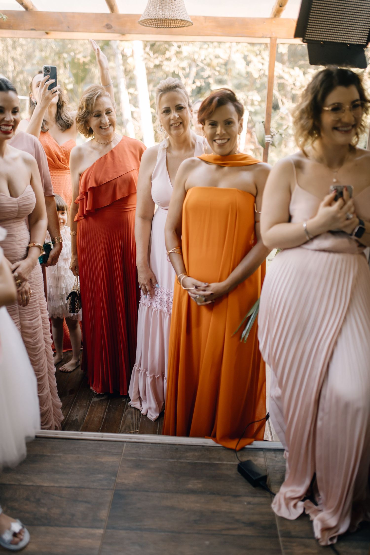 Bridesmaids wear mix of orange, coral, and blush floor-length dresses at wedding celebration.