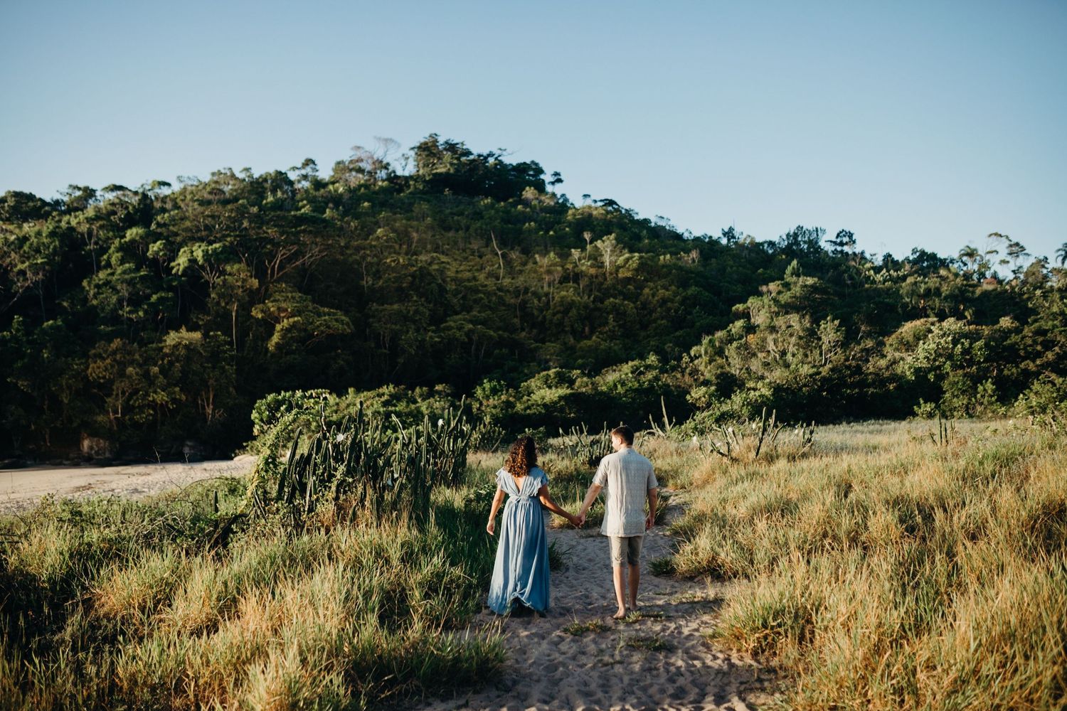 Couple walking hand in hand on hiking trail through scenic mountain landscape.