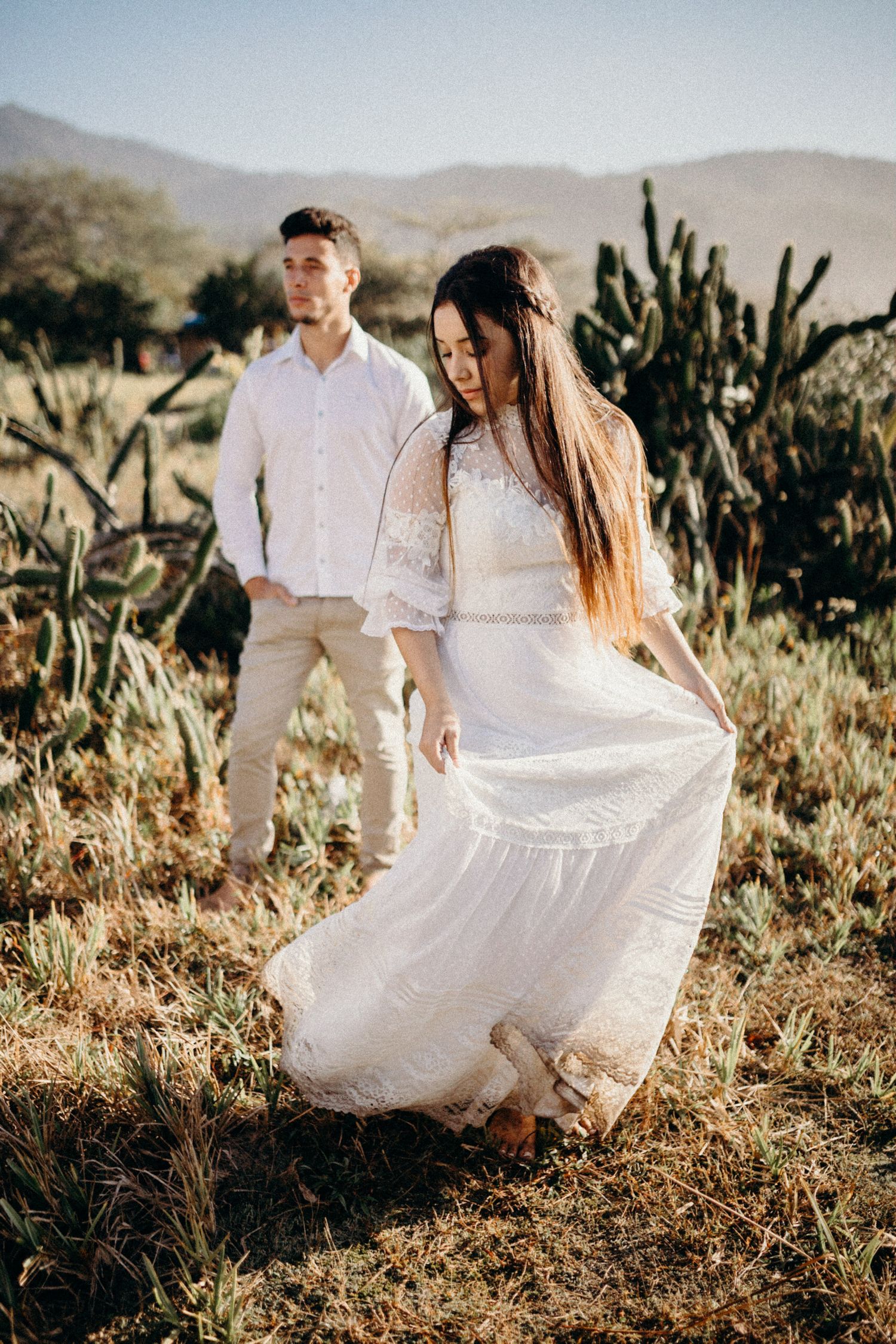 Desert photoshoot featuring flowing white dress against mountain landscape with cacti.