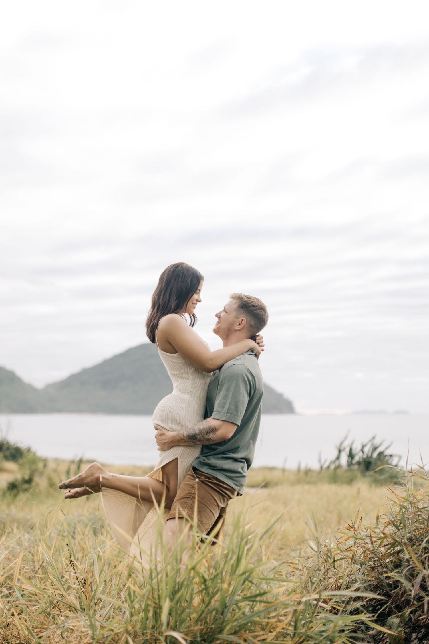 Two people embrace passionately while standing in a field with mountains visible in the distance.