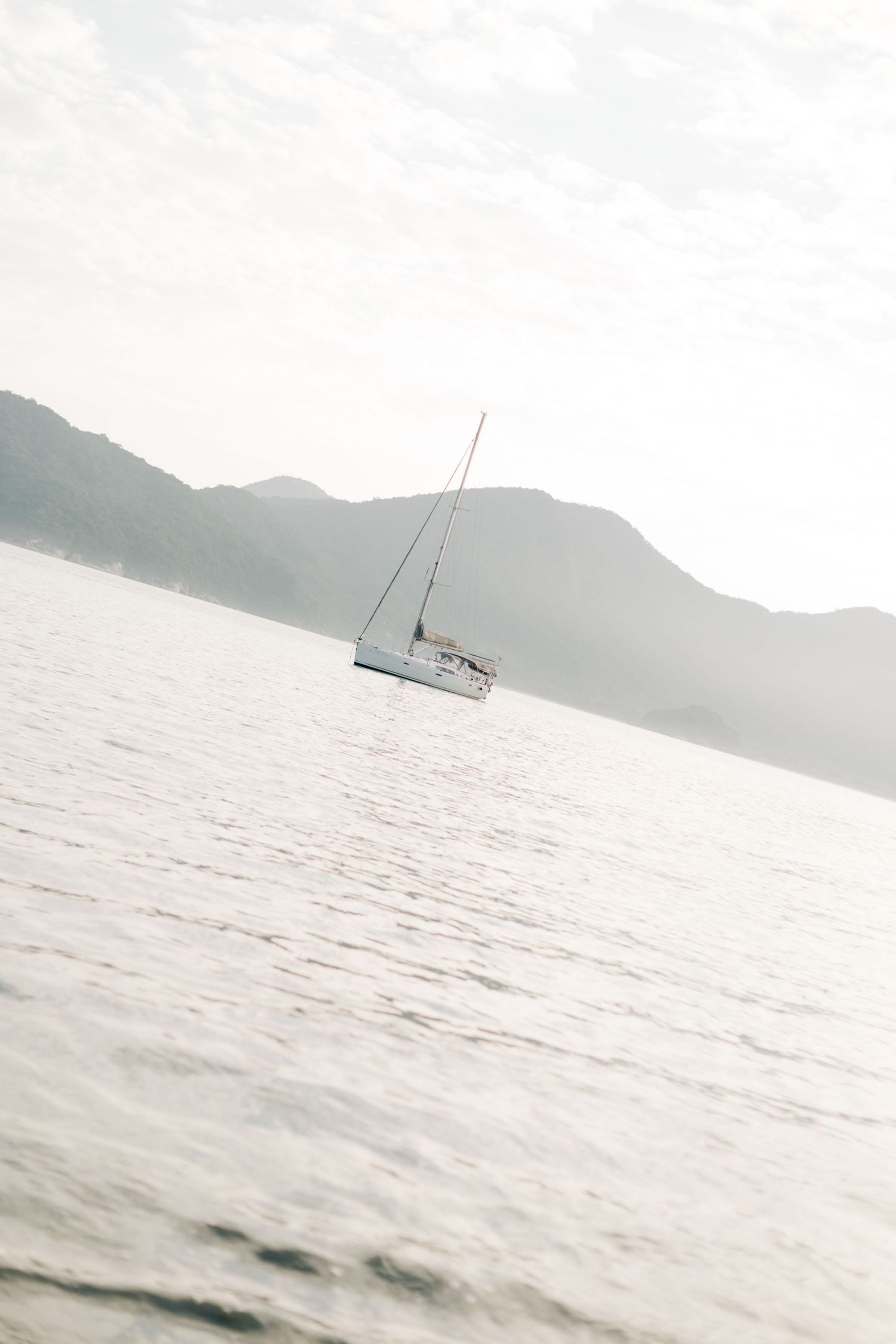 A sailboat floating peacefully on calm waters with misty mountains in the background.