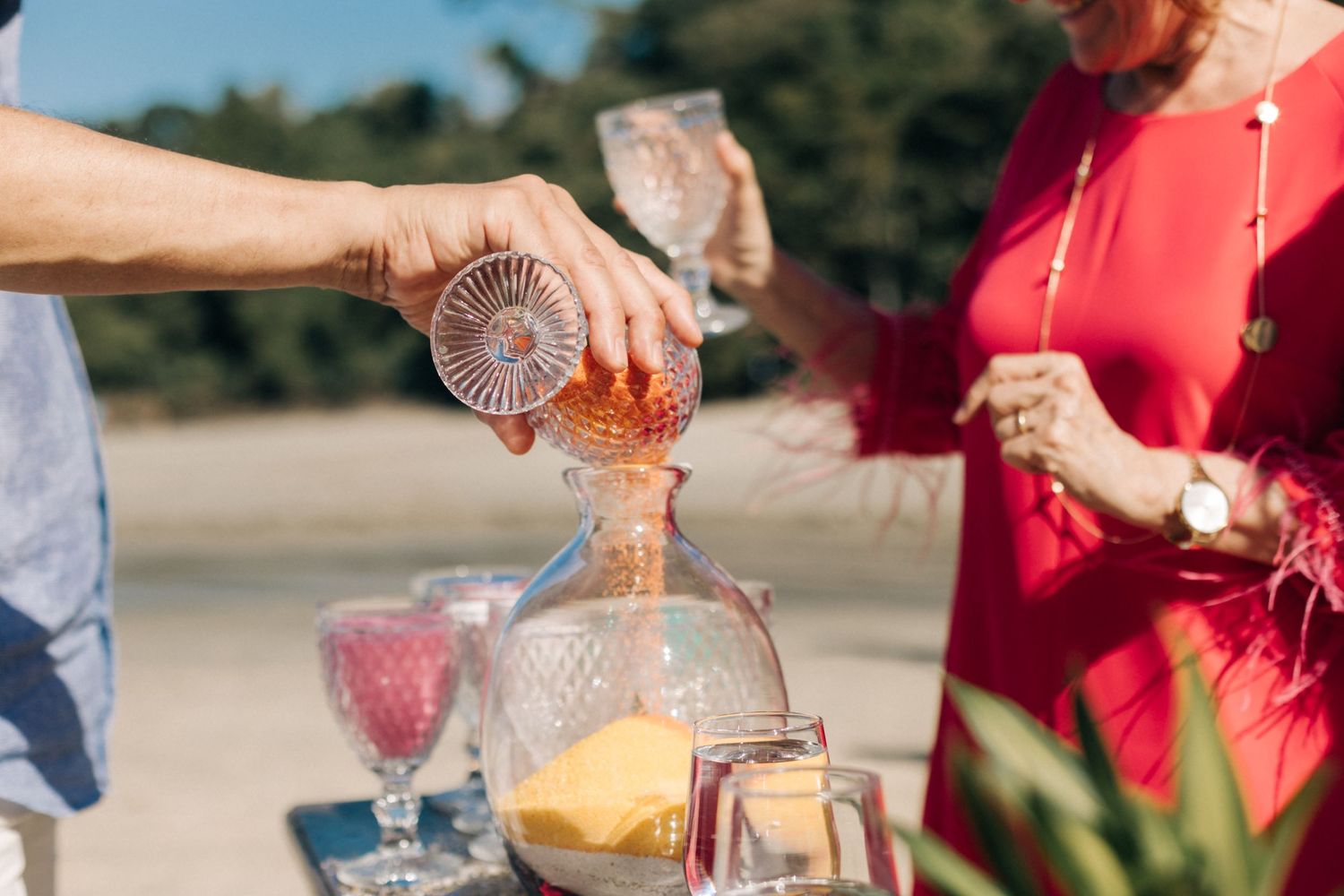 Person pours orange liquid into decorative glass vessel at outdoor event.