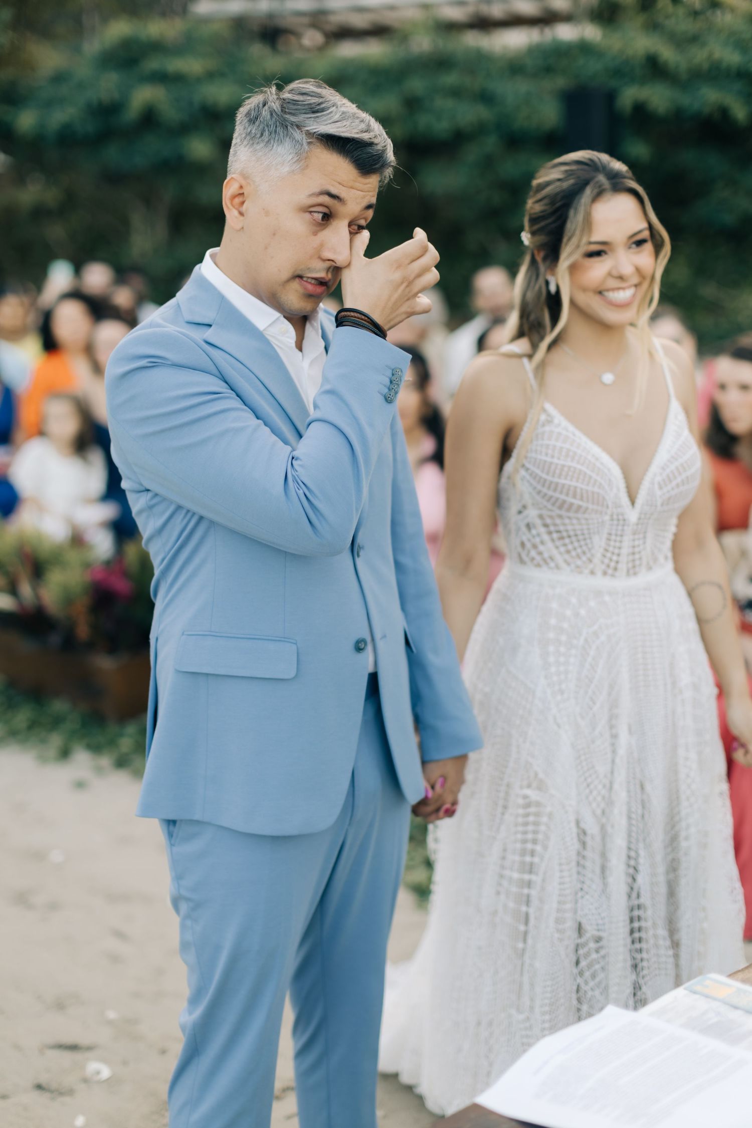 Wedding couple in light blue suit and white lace dress at outdoor reception.