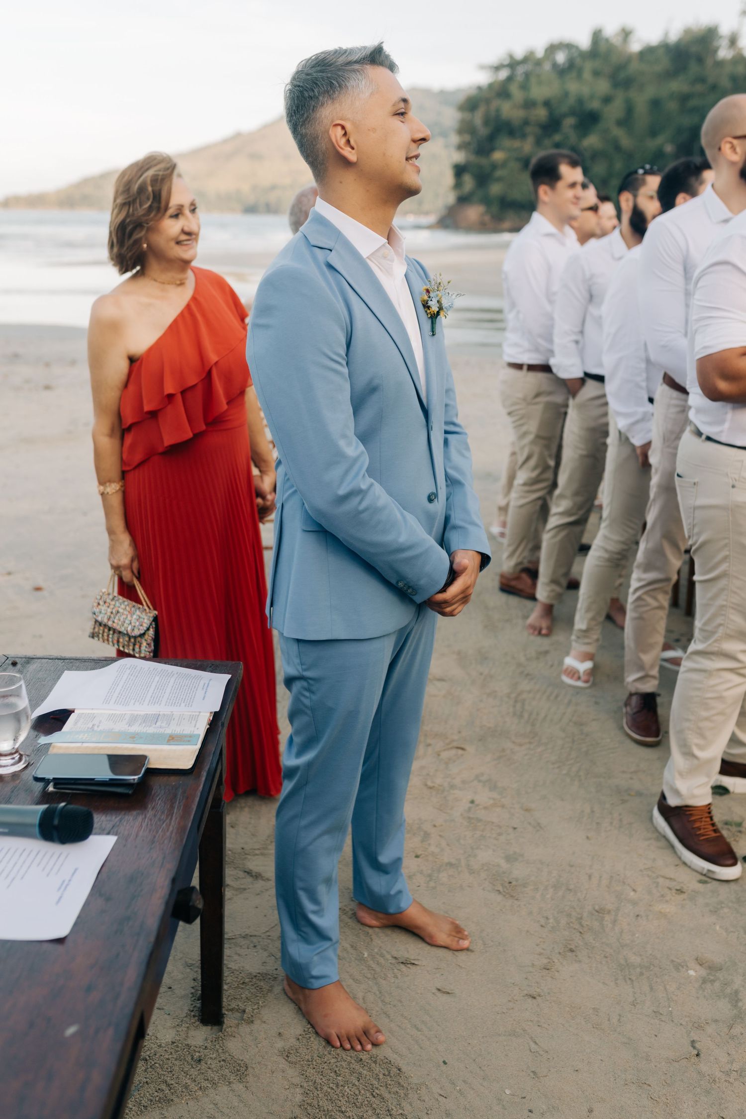 Wedding ceremony on beach with attendant in light blue suit and red dress.