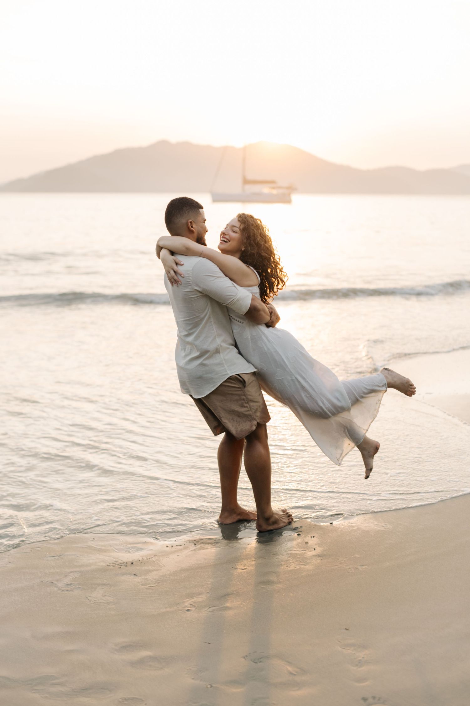 Joyful beach engagement photo with couple spinning in sunset light.