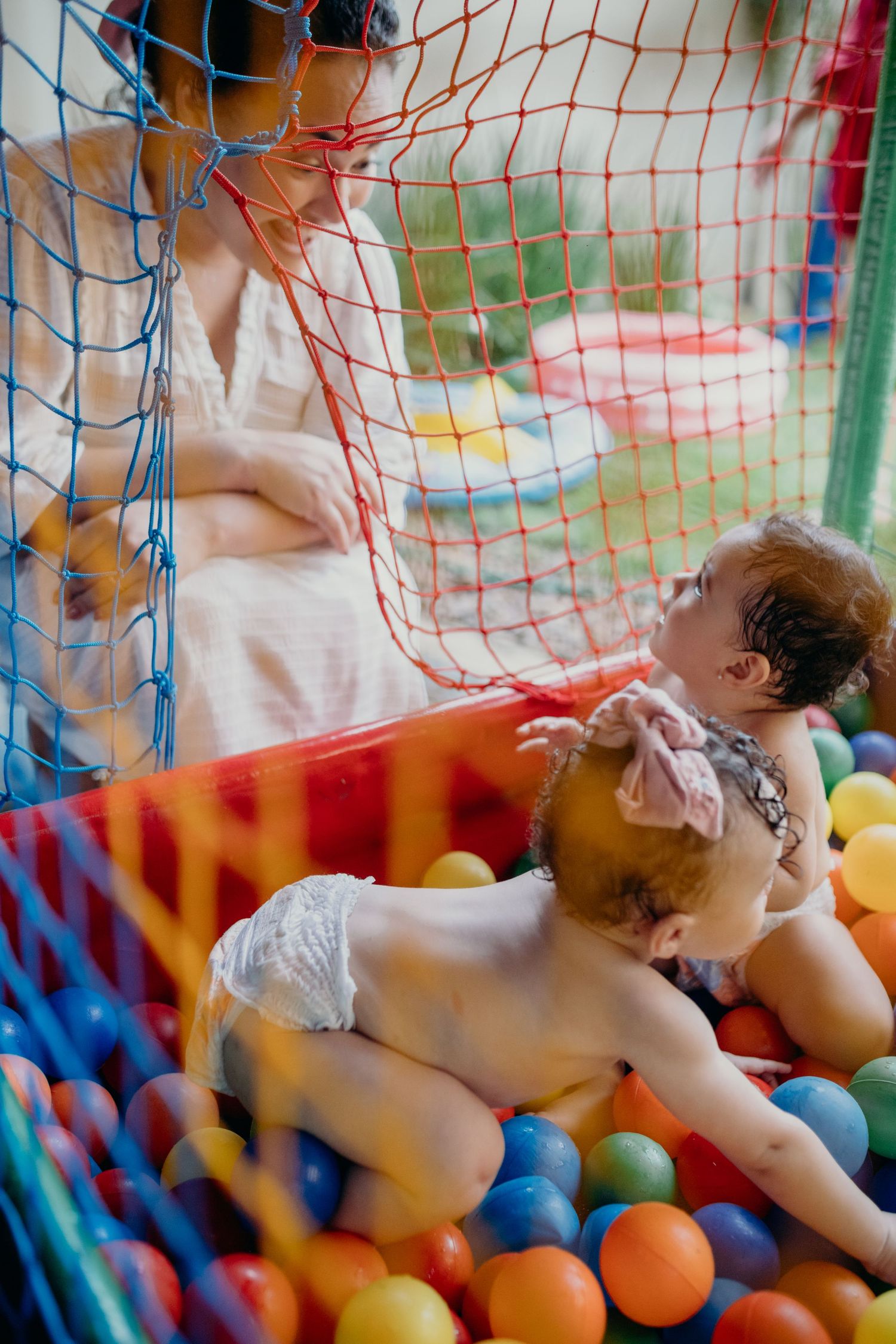 Children playing in a colorful ball pit with netting at an outdoor playground.