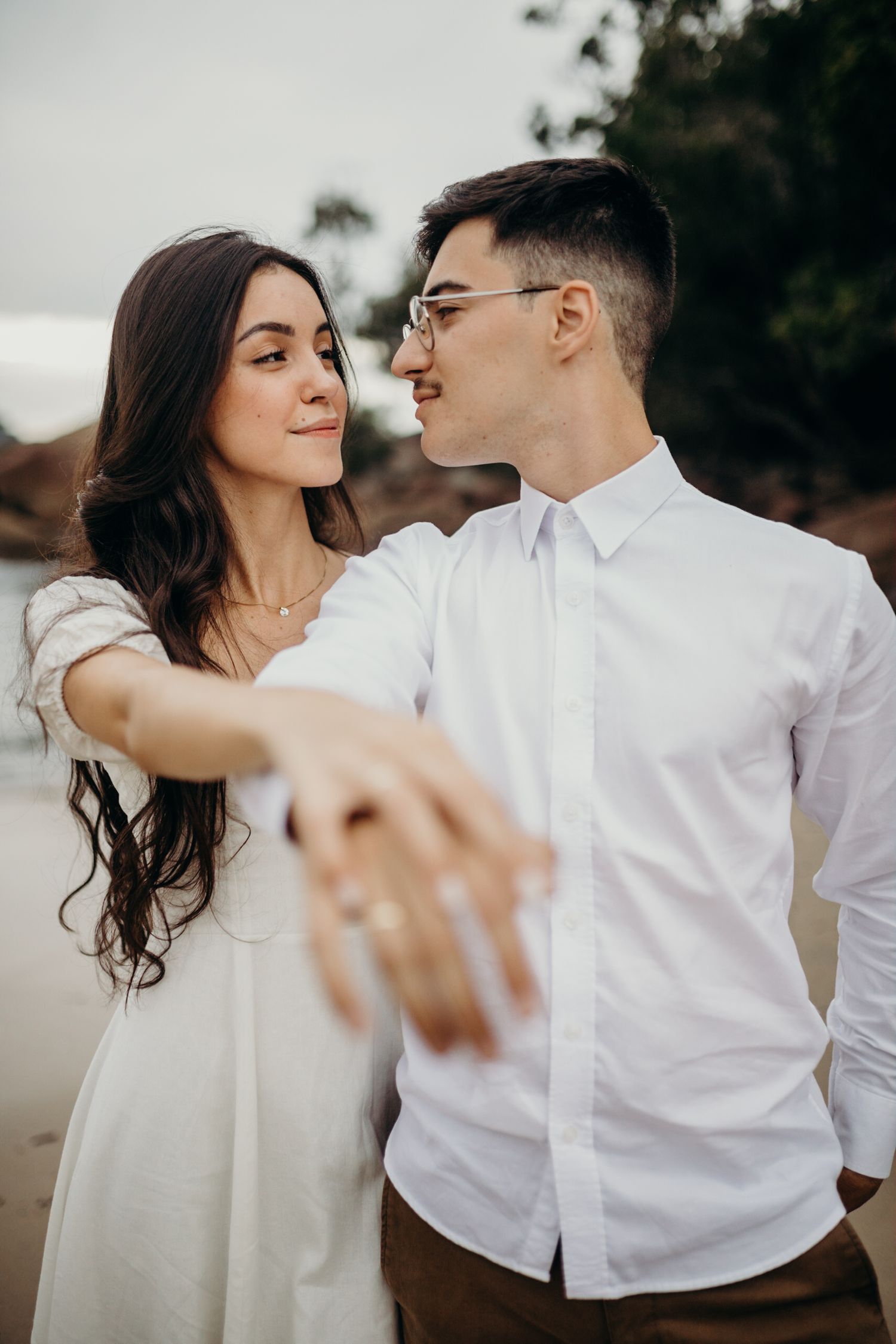 A couple in white clothing shares romantic dance poses during their beach photoshoot.
