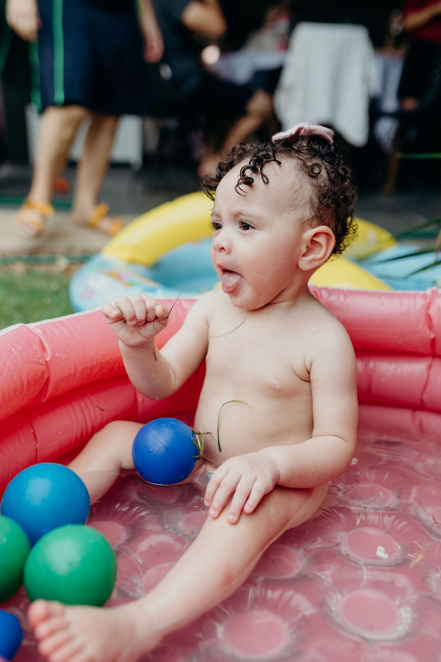 Inflatable pink pool with colorful balls on green grass.