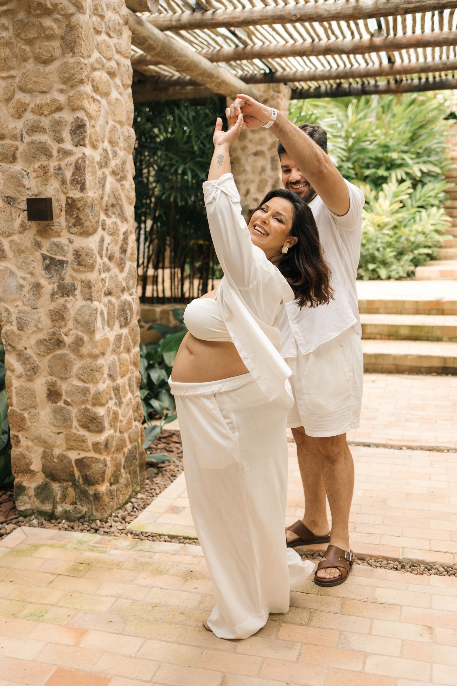 A couple in white outfits dancing together under a stone archway in a romantic outdoor setting.