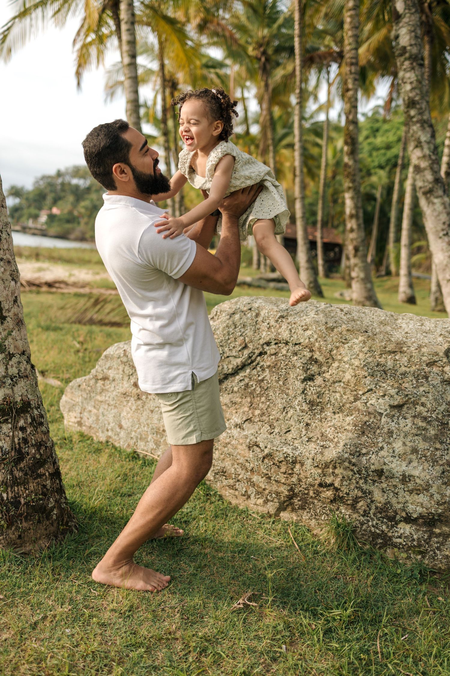 A playful scene among palm trees as a parent lifts a small child in the air on a grassy slope.
