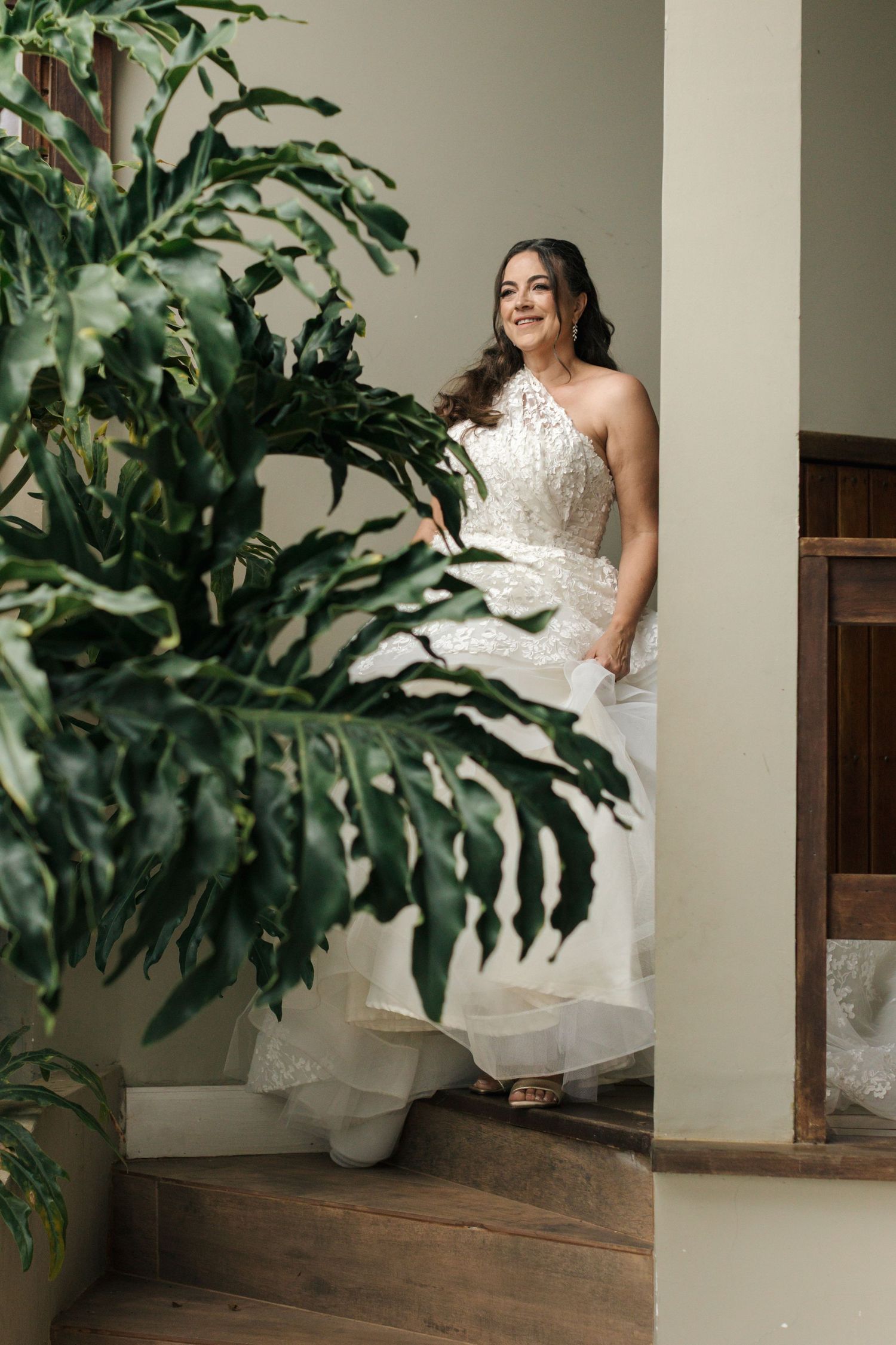 A white wedding dress detail shot with tropical monstera leaves in an indoor setting.