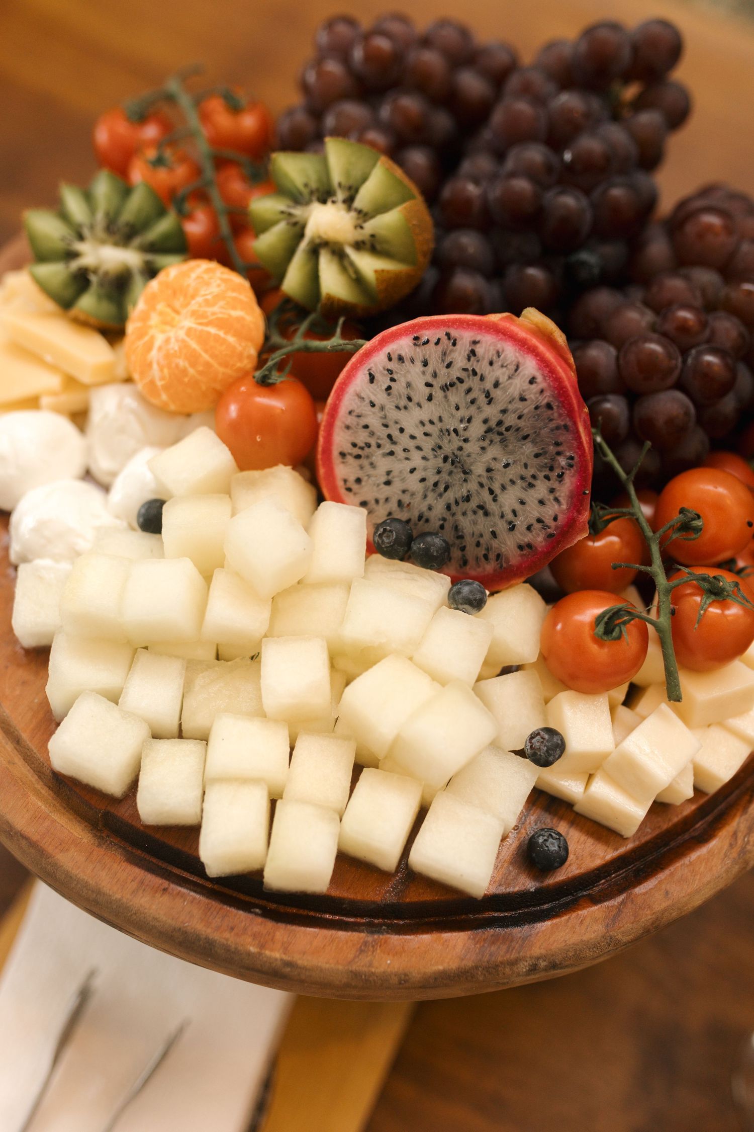Wooden platter with cubed cheese, dragon fruit, grapes and fresh berries.
