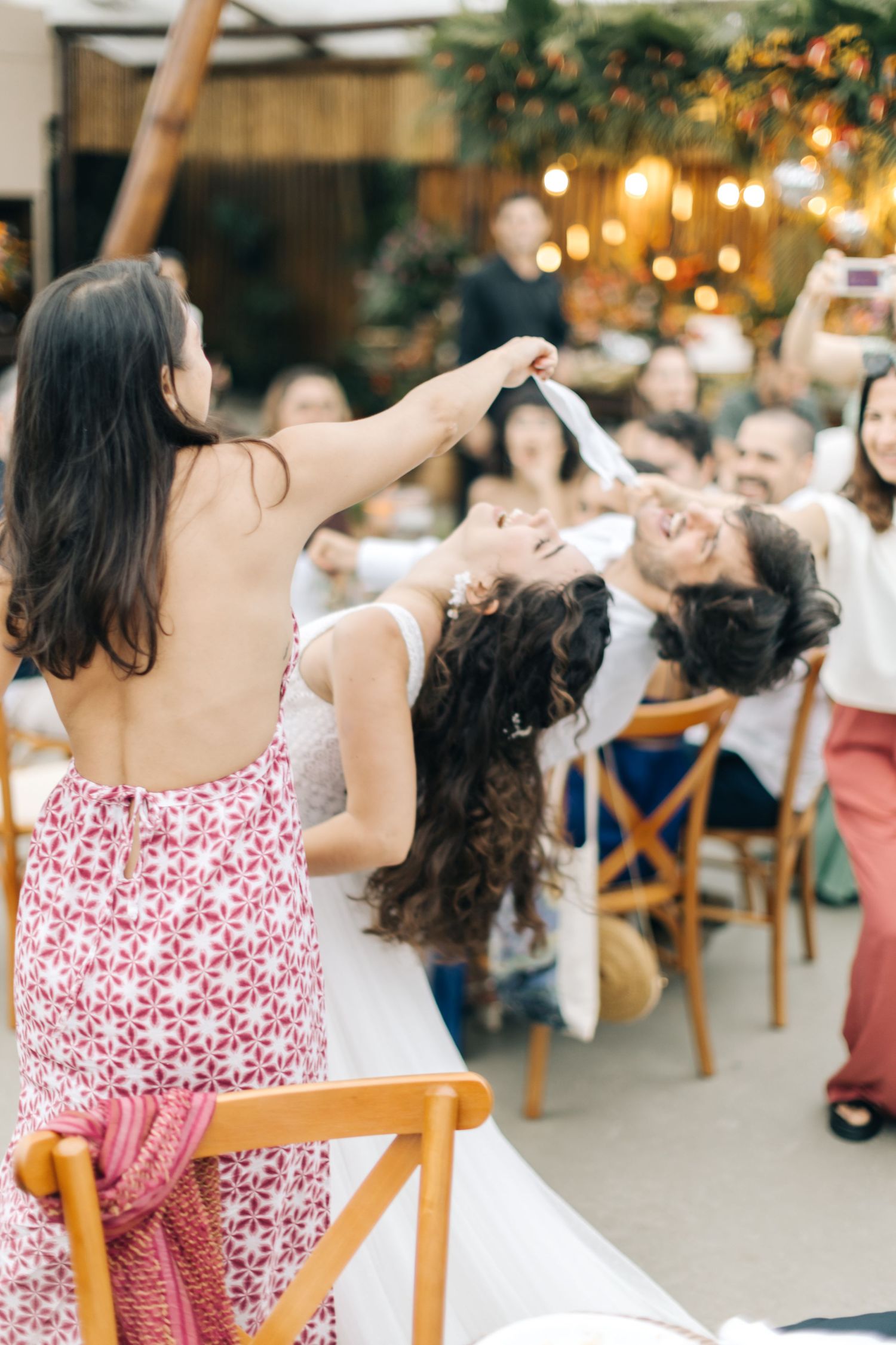 Wedding guests participate in lively party game at reception under string lights.