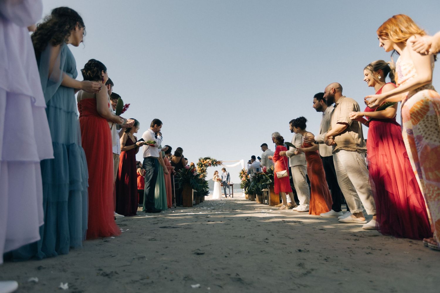 Wedding guests line sandy aisle with cameras during beachfront ceremony.