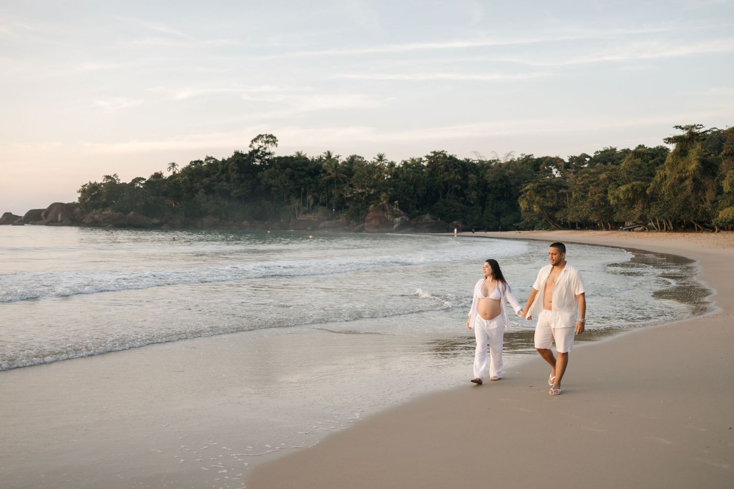 Couple taking romantic walk along pristine beach with tropical forest backdrop.